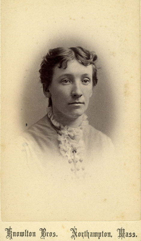 A younger Cornelia M. Clapp against a gray circular background. Her skin is fair, with her brown hair pulled back. She wears a collared dress. Text on the bottom reads "Knowlton Bros. Northampton, Mass."