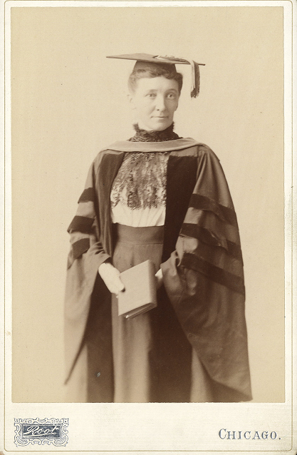 Cornelia M. Clapp posing in PhD robes with a collared dress underneath, while holding a book. She looks towards the camera with a slight smile. The background is a plain light grey. Text at the bottom of the photograph reads "Root. CHICAGO."