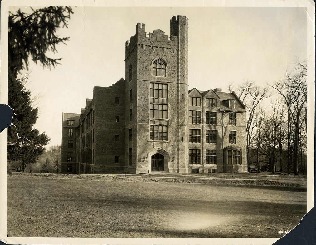 A view of the front of Clapp Building from a slight angle. The building is surrounded by trees without leaves. The scanned photograph has damages on the middle left side and the bottom left corner.