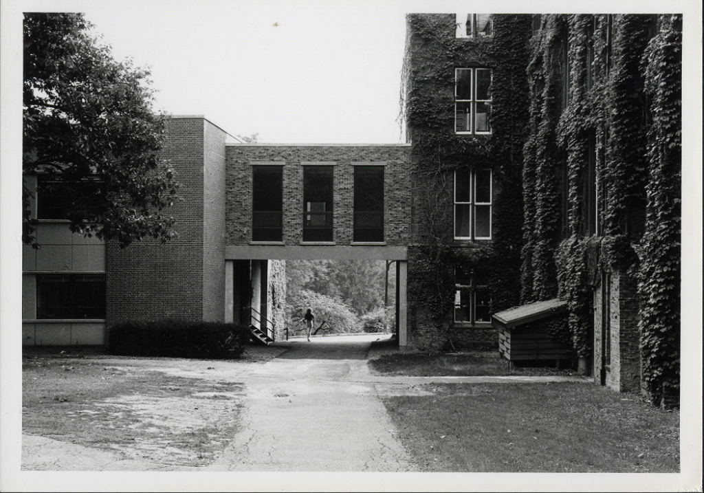 The brick skybridge with three windows that connects Carr and Clapp buildings. A person walks on the path under the bridge.