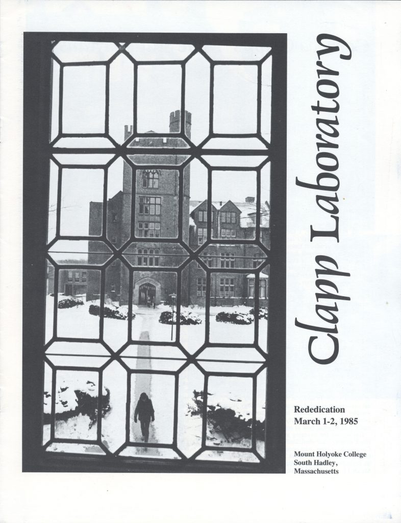 Clapp Laboratory viewed through a window. Snow is on the ground, with someone walking on a path. Text to the left reads "Clapp Laboratory. Rededication March 1-2, 1985. Mount Holyoke College, South Hadley, Massachusetts."