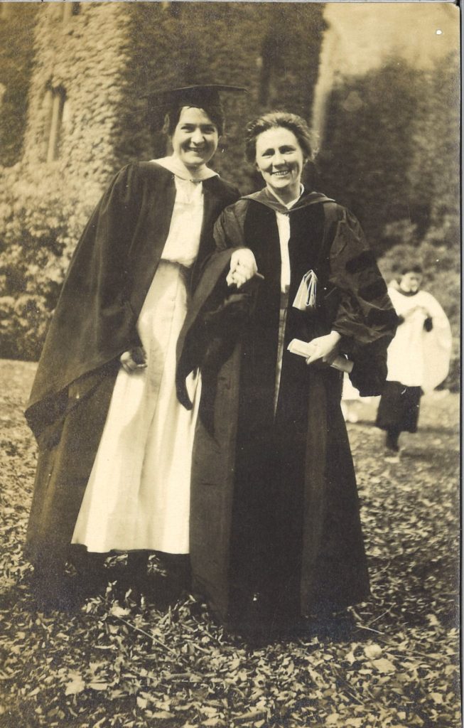 Two women pose outside in graduation robes.