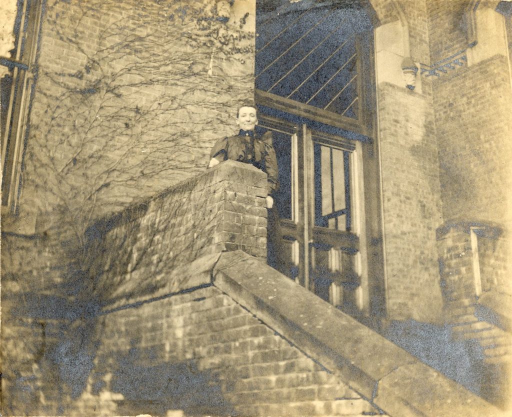 A woman stand atop a staircase in front of an ivy covered brick building