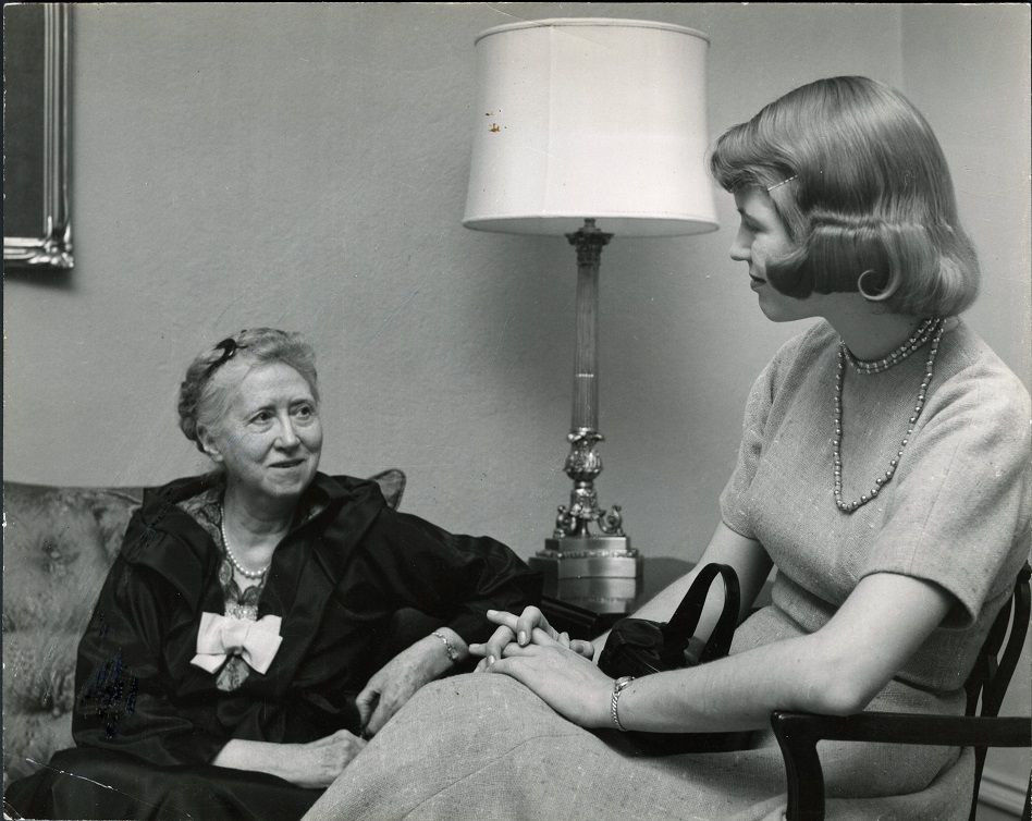 Moore and Plath in conversation. Moore is seated on a couch and Plath beside her in a chair.