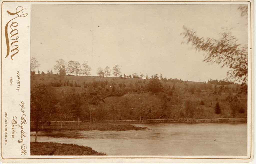 A lake with a hill behind. A small structure is at the top of the hill in the distance.