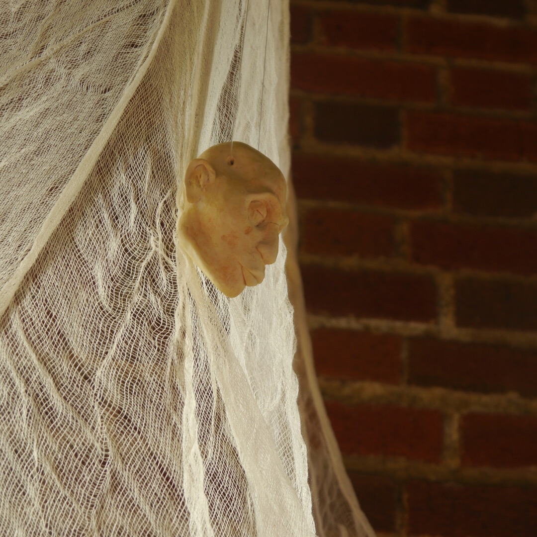 picture of a white clay head hanging with cheesecloth with a brick wall behind it