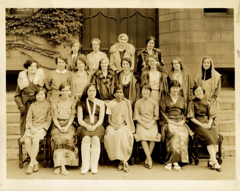 Three rows of international students (19 individuals in total) outside a stone staircase, wearing traditional cultural clothing.