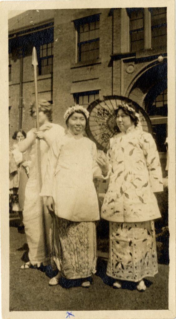 Yau Tsit Law, class of 1916, and Chi Nyok Wang, class of 1916, are dressed in traditional Chinese attire and holding a parasol. Yau Tsit Law is the person to the left. 1916.
