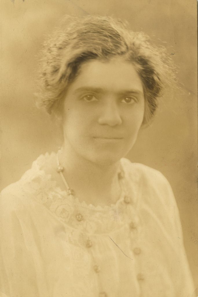 Rosa Yerenian stares into the camera, wearing a white lace gown with a delicate necklace.