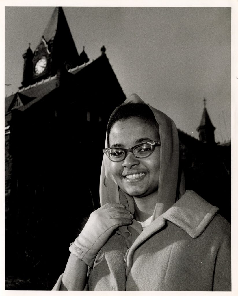 Grayscale photo of Raga Mohommad smiling, standing on Mount Holyoke's campus, in front of the clock-tower.