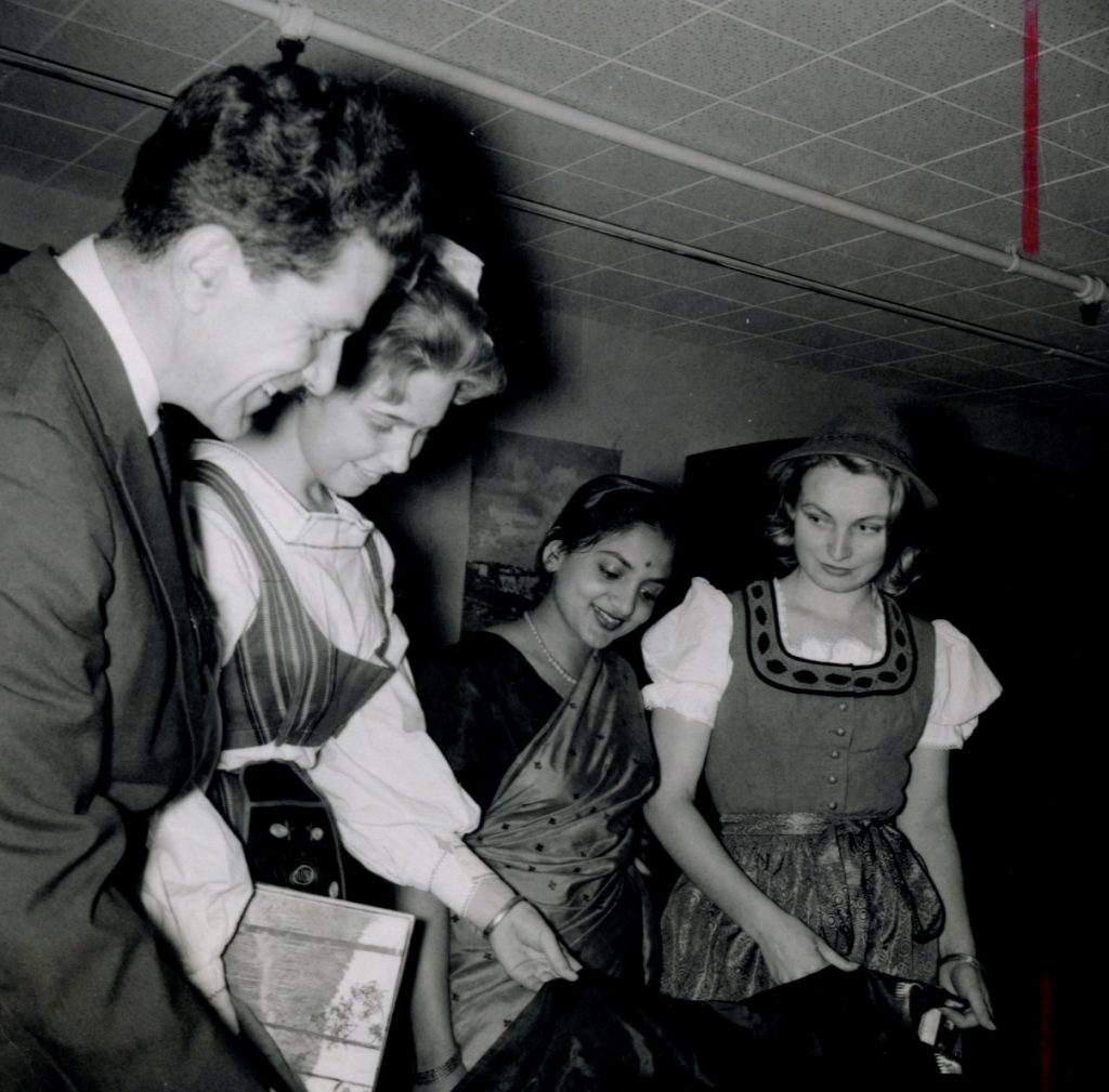 A suited professor and three students in cultural dress gather and exchange smiles.