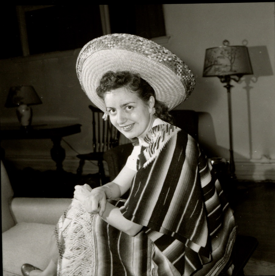 A smiling student dressed in a striped Mexican poncho and a sombrero sits on a sofa.