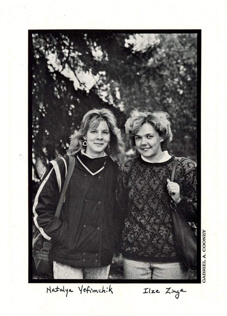 Two students in sweaters with a background of pine trees.