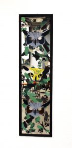 A mirror hangs on a wall.  Three owl faces are printed on paper and placed on the mirror. The actual mirror is covered in the same owl faces but in shades of green to mimic leaves.