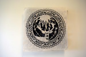 Square piece of kozo paper hanging several inches away from the wall. An image of a deer surrounded by other details is cut out of it. Behind it, on the wall is a and equally sized piece of dyed black kozo paper which is slightly crumpled