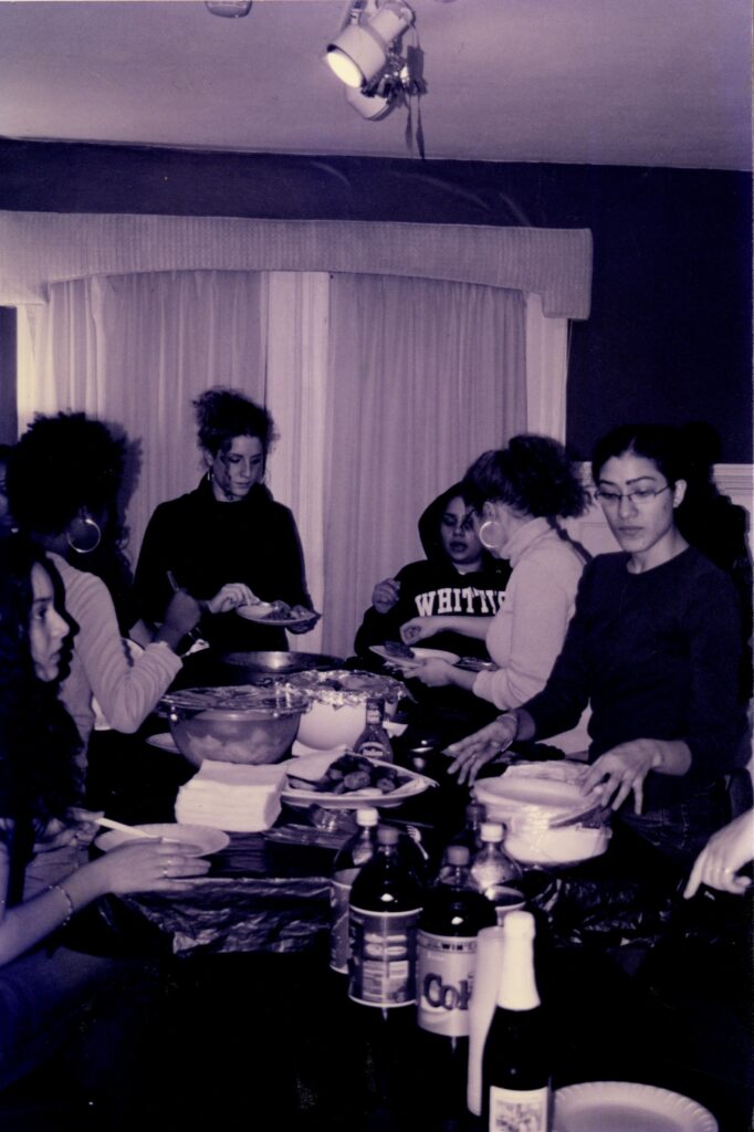 A black and white photograph of people standing around a table serving themselves plates of food