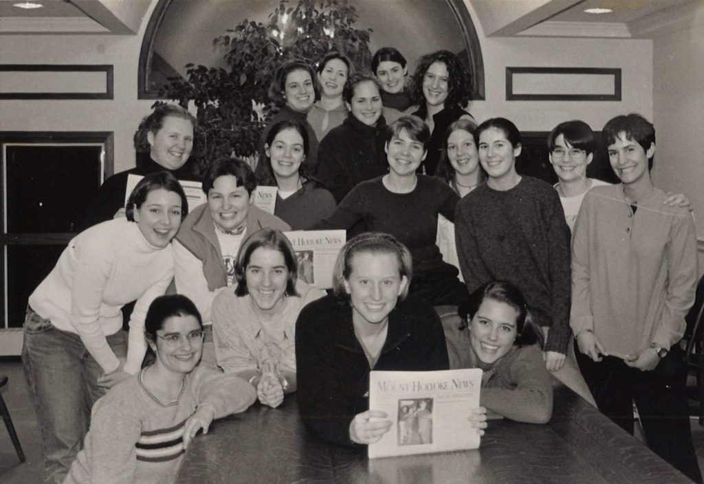 A group of Mount Holyoke students stand together smiling. A few of the students are hold up copies of The Mount Holyoke News.