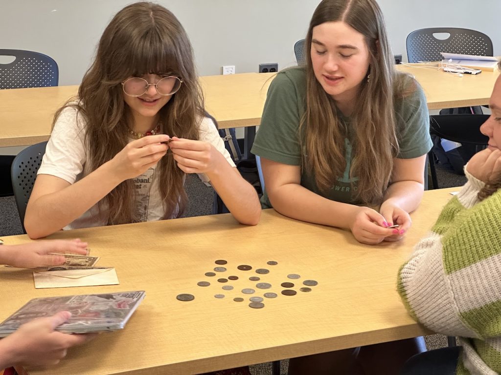 Two students looking closely at a set of coins.