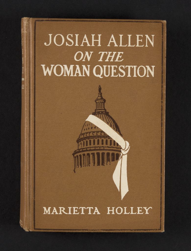 The book’s cover is a sandy brown color accented by dark brown and white. A dark brown line follows the book’s perimeter. The title and author are displayed in large white script at the top and bottom of the cover, respectively. In the center, the dome of the United States Capitol Building is rendered in dark brown, with a bold white sash tied diagonally across the dome, tied at right.