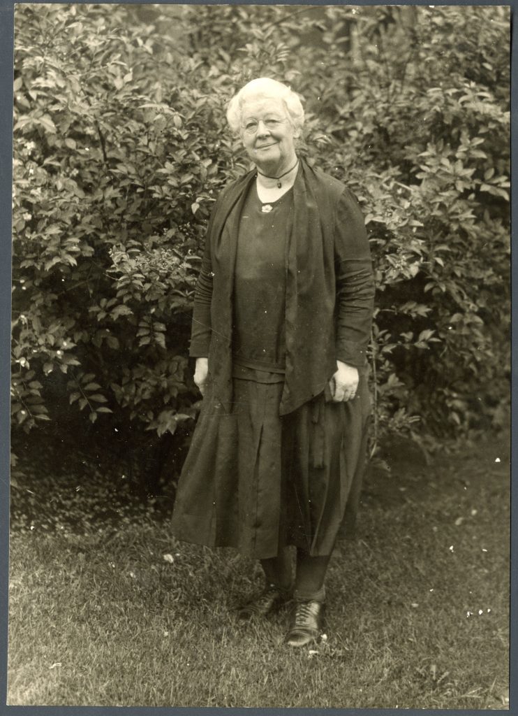 Black and white photograph of Miller standing in front of a large bush