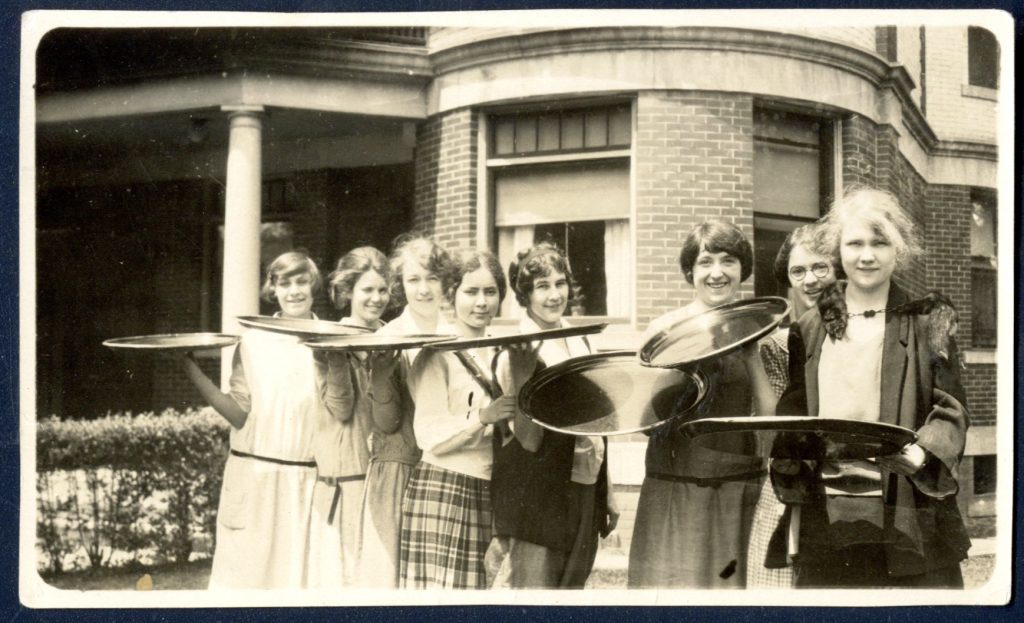 A group of students stand outside a brick building holding serving trays