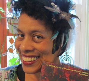 Andrea Hairston, wearing a feathered hairpiece and holding a book.